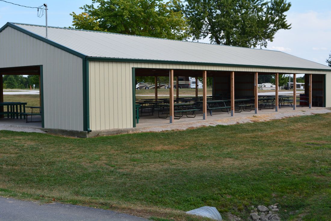 A pavilion with tables and chairs inside of it is sitting in the middle of a grassy field.