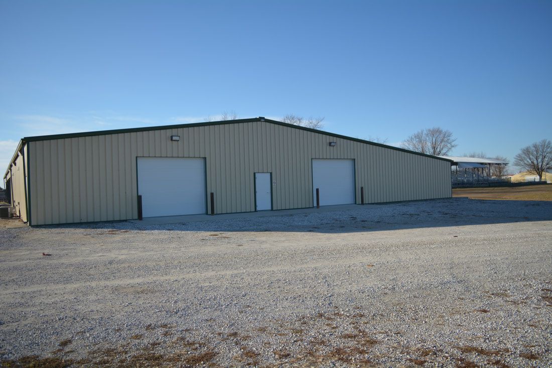 A large metal building with white doors is sitting on top of a gravel road.