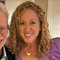 A man and a woman are posing for a picture together . the woman is wearing a purple shirt and a necklace.