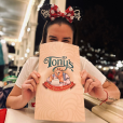 A woman is sitting at a table holding a tony 's bag in front of her face.
