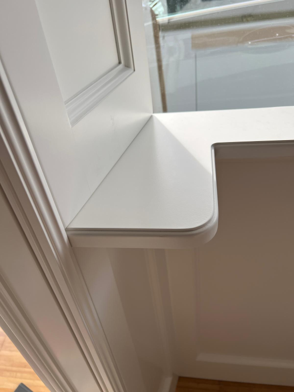 Sedile o mensola bianca accanto a una porta chiusa, con luce solare che illumina una parete interna beige.