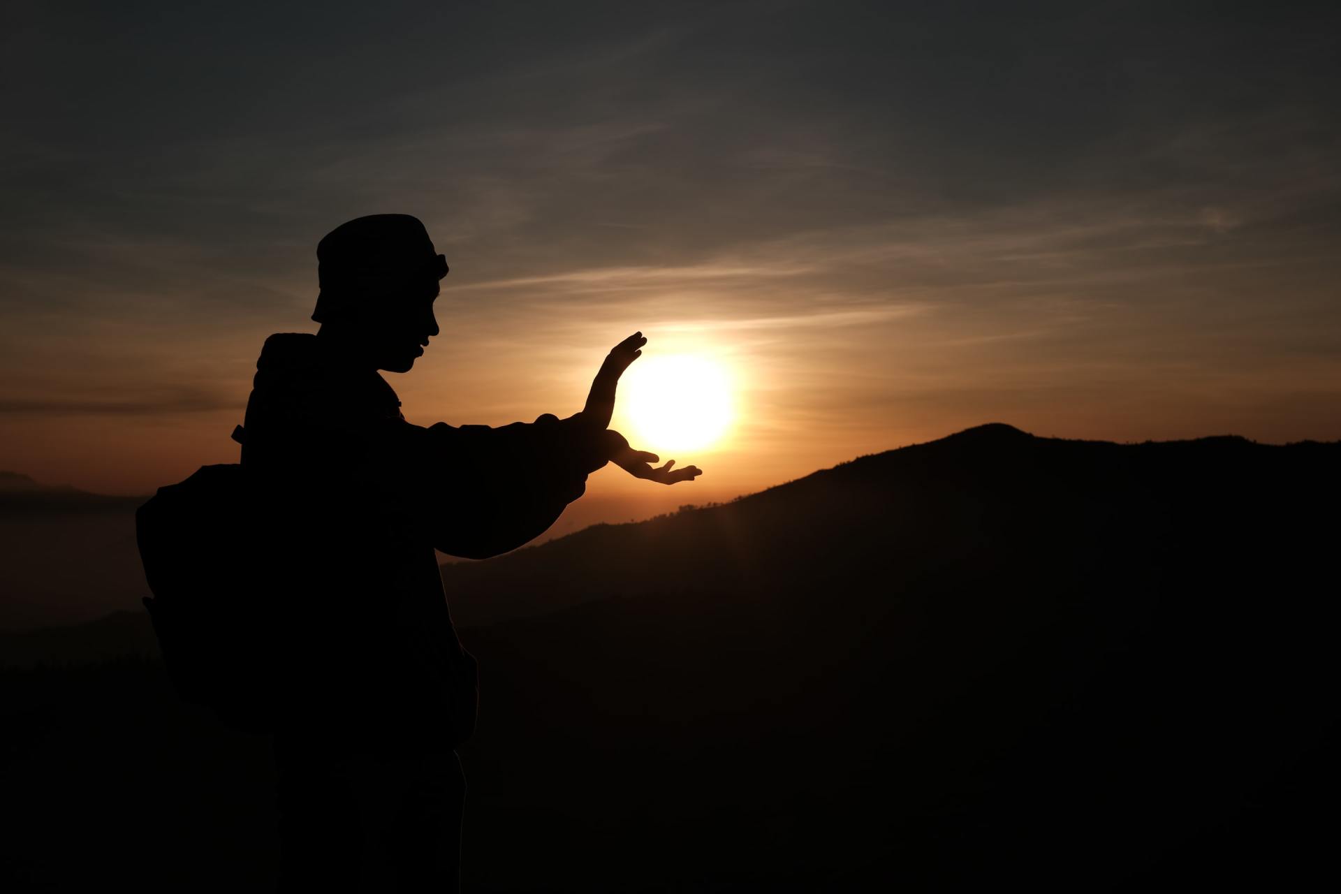 A silhouette of a person holding the sun in their hand