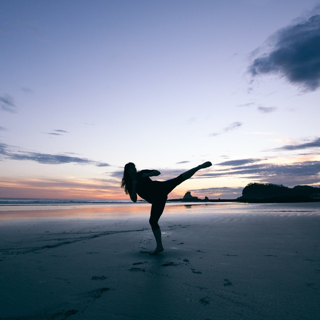 A silhouette of a woman kicking on a beach at sunset