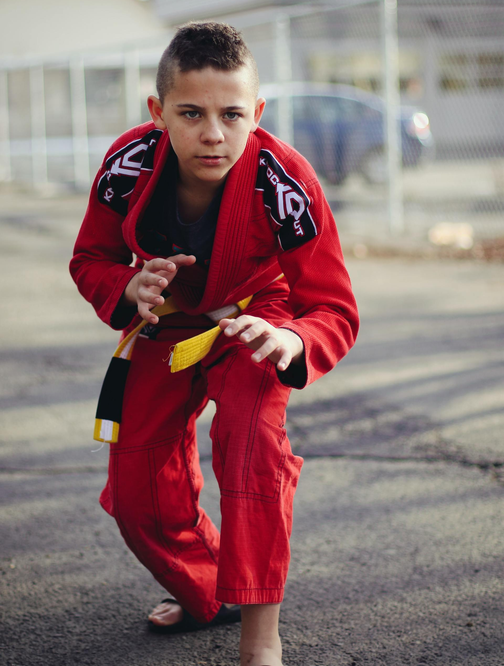 A young boy wearing a red karate uniform is squatting down