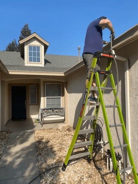 A man standing on a green ladder in front of a house