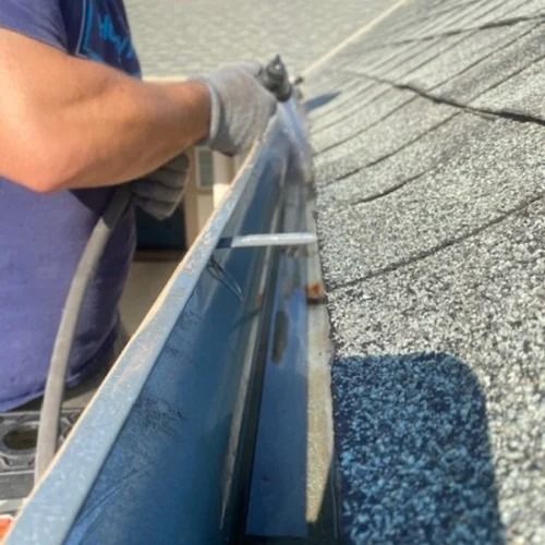 A man is working on a gutter on a roof.