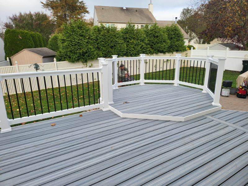 White deck with curved railing, gray flooring, and a backyard view with grass, hedge, and house.