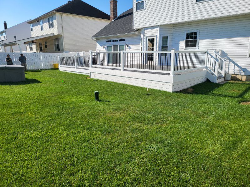 White house with raised deck and stairs overlooking a green backyard under a clear blue sky
