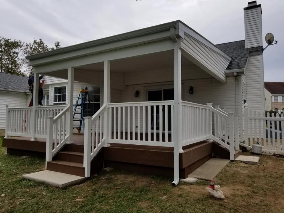 Porch with white railings and steps on a small house, viewed from the yard.
