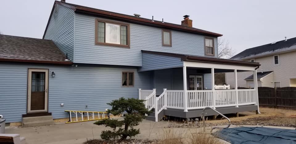 Blue two-story house with white porch railing and a small tree in the front yard