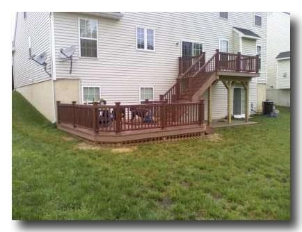 Backyard with a wooden deck and stairs attached to a beige house, overlooking a grassy lawn