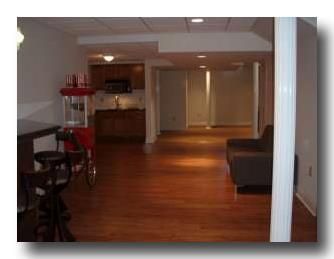 Empty living room with hardwood floors, sofa, and a red cart near a kitchen area