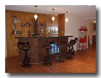 Home bar with granite countertop, four stools, hanging lights, and warm wood flooring