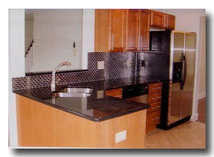 Modern kitchen with wood cabinets, black countertop, stainless sink, and black tile backsplash.