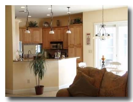 Bright kitchen and living area with wood cabinets, pendant lights, and a couch in the foreground