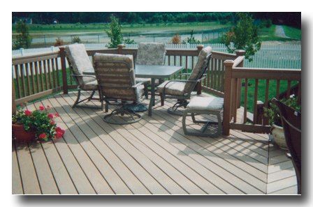 Wooden deck with patio chairs and a round table, overlooking a fenced yard and pond.