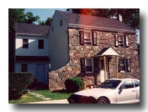 Stone-front suburban house with a parked white car in front and trees behind.