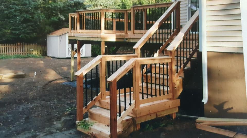 Wooden outdoor stairs and landing beside a house, with railings and a small fenced porch.