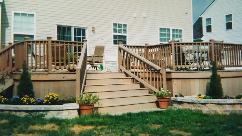 Backyard deck with wooden stairs, potted plants, and patio furniture beside a beige house