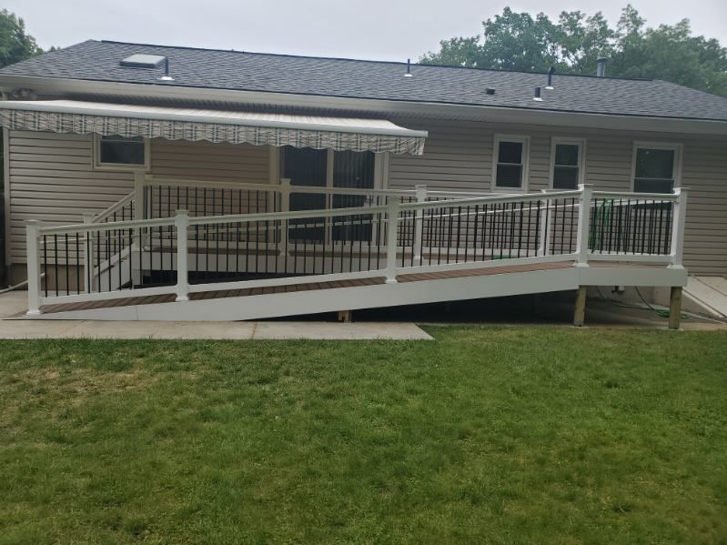 House with wheelchair ramp and white railing leading to a porch, front lawn in foreground