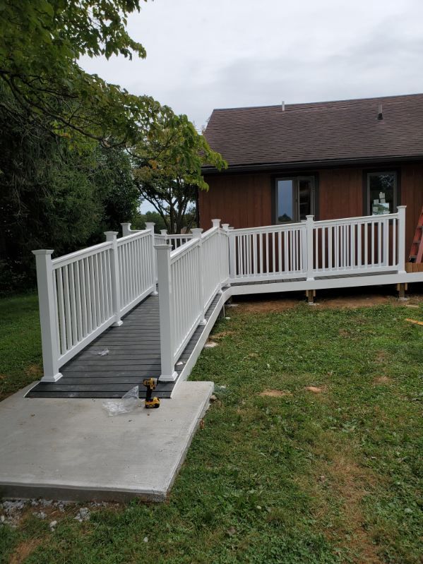 White accessibility ramp with railings leading to a house deck beside a grassy yard.