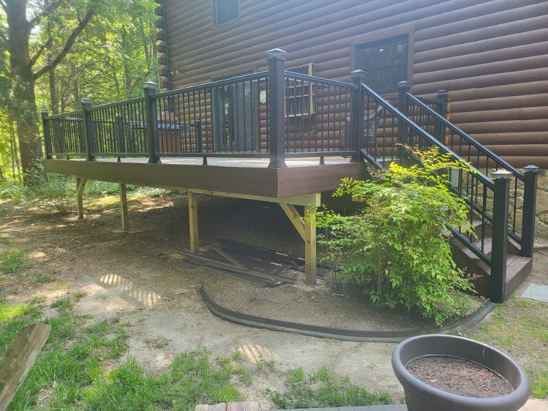 Raised wooden deck with black railings and stairs beside a log cabin in a wooded yard