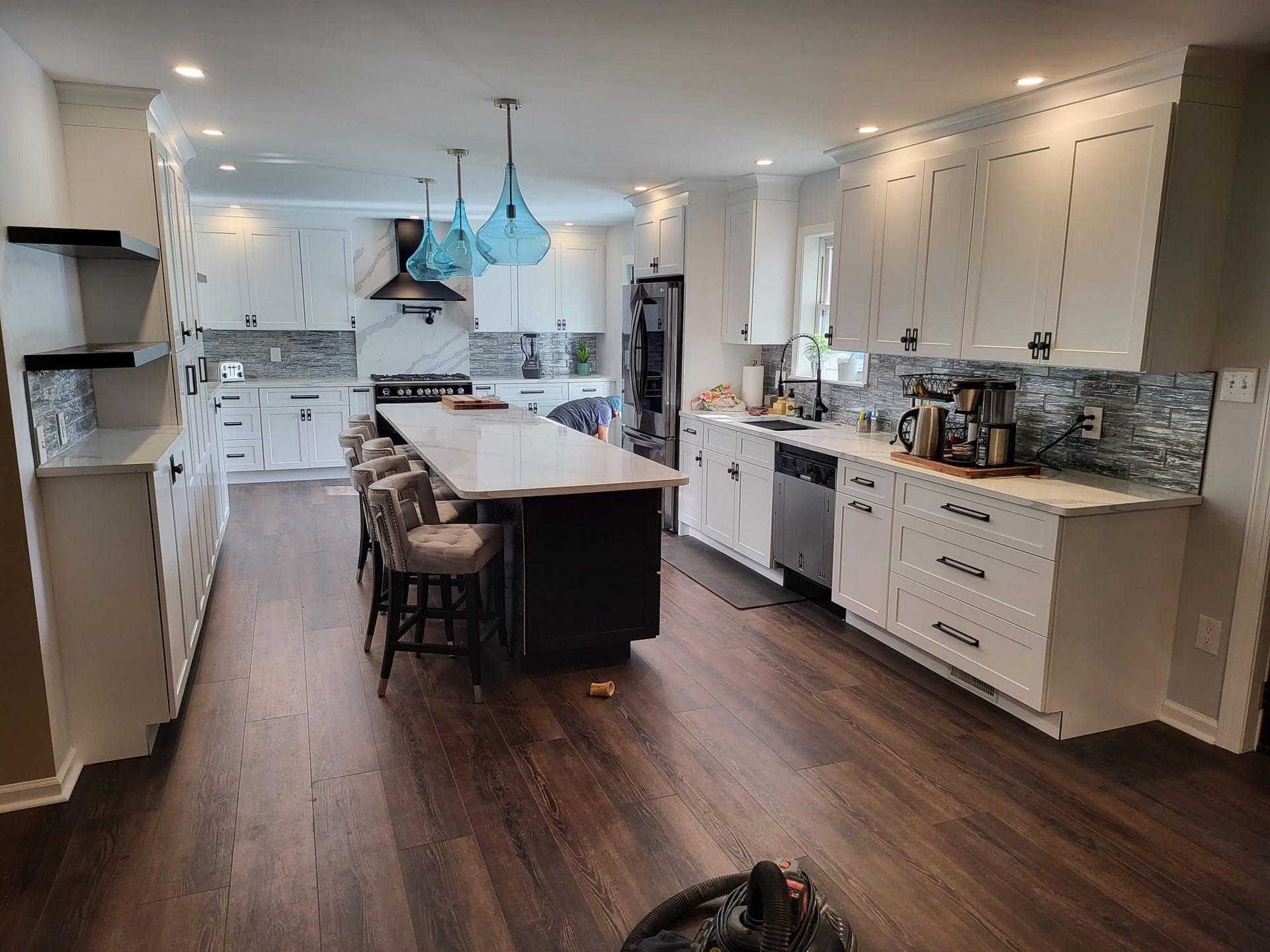 Modern white kitchen with large island, blue pendant lights, dark wood floor, and stainless appliances
