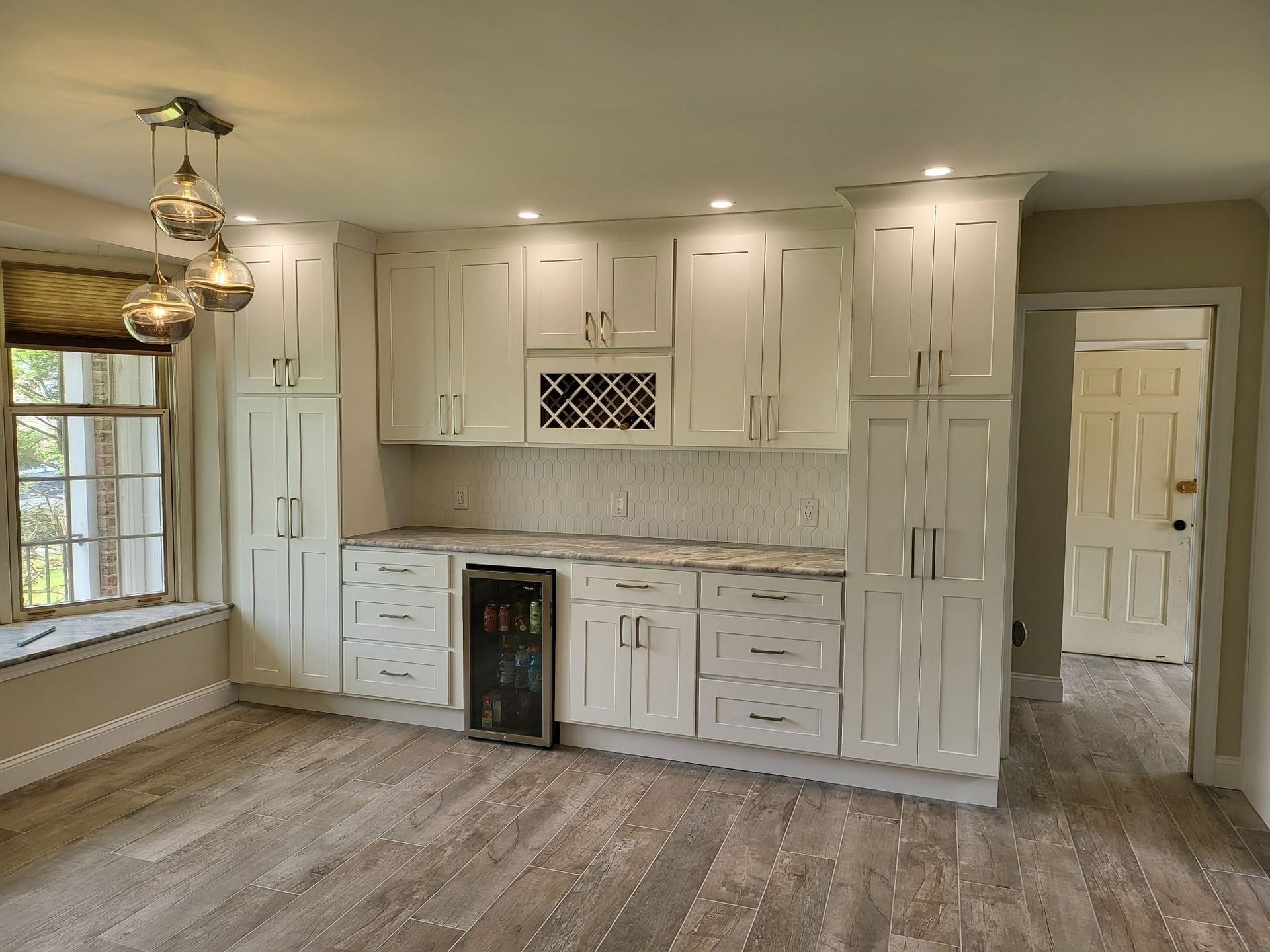 Bright kitchen with white cabinets, marble backsplash, wine fridge, and wood-look flooring