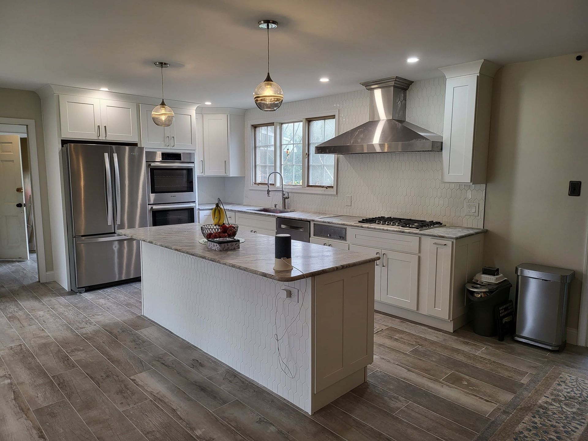 Modern white kitchen with island, stainless steel appliances, pendant lights, and wood-look flooring