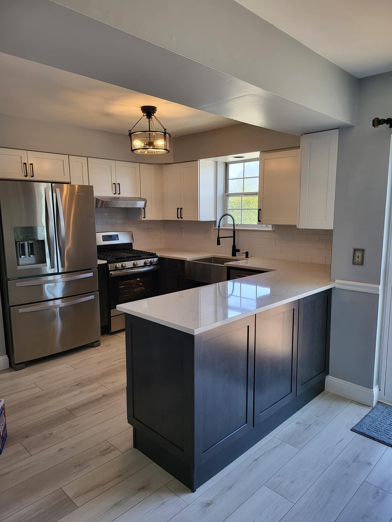 Modern kitchen with stainless steel appliances, white cabinets, and a dark island beneath a pendant light