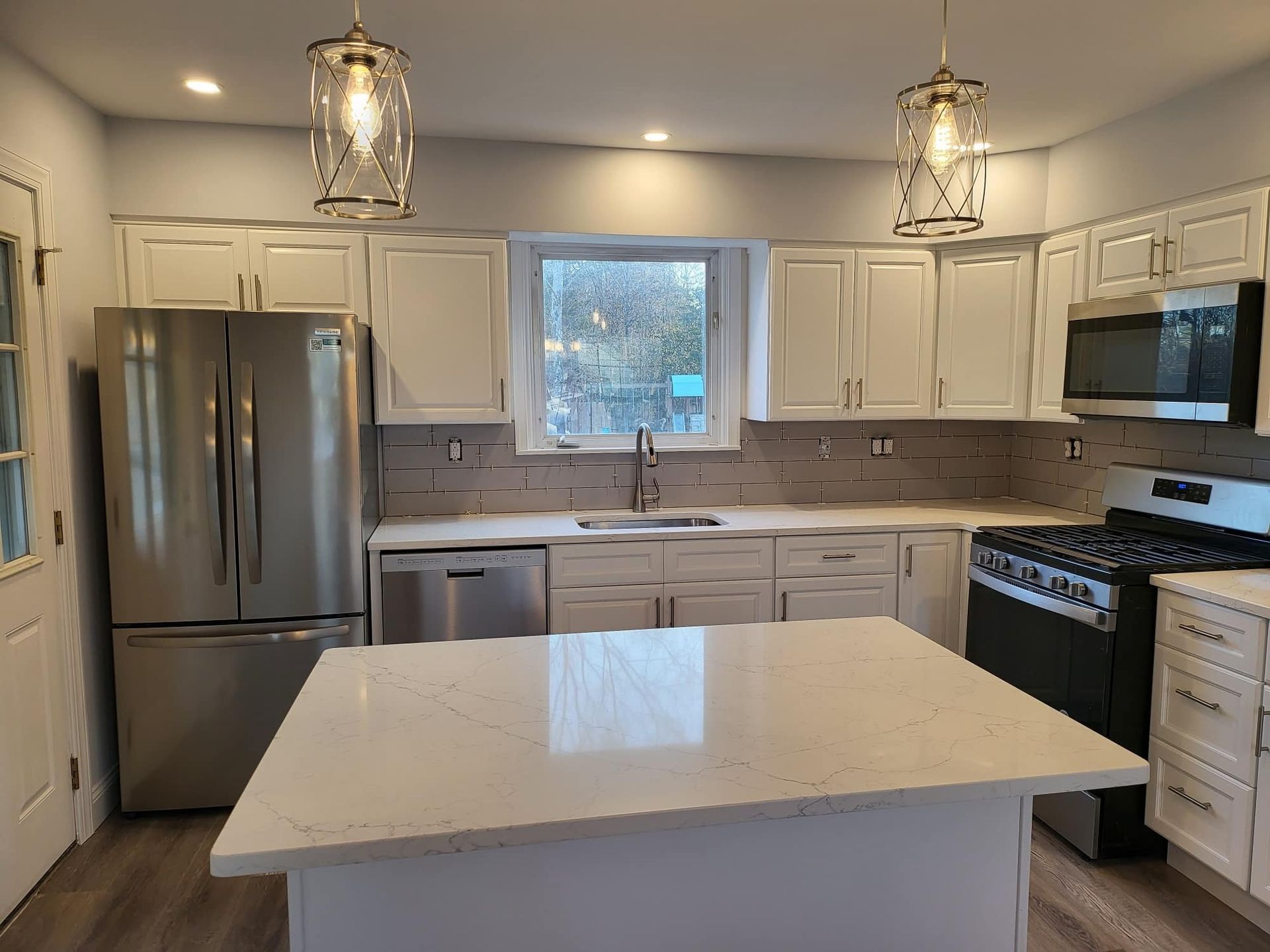Bright white kitchen with island, stainless steel fridge, farmhouse sink, and pendant lights