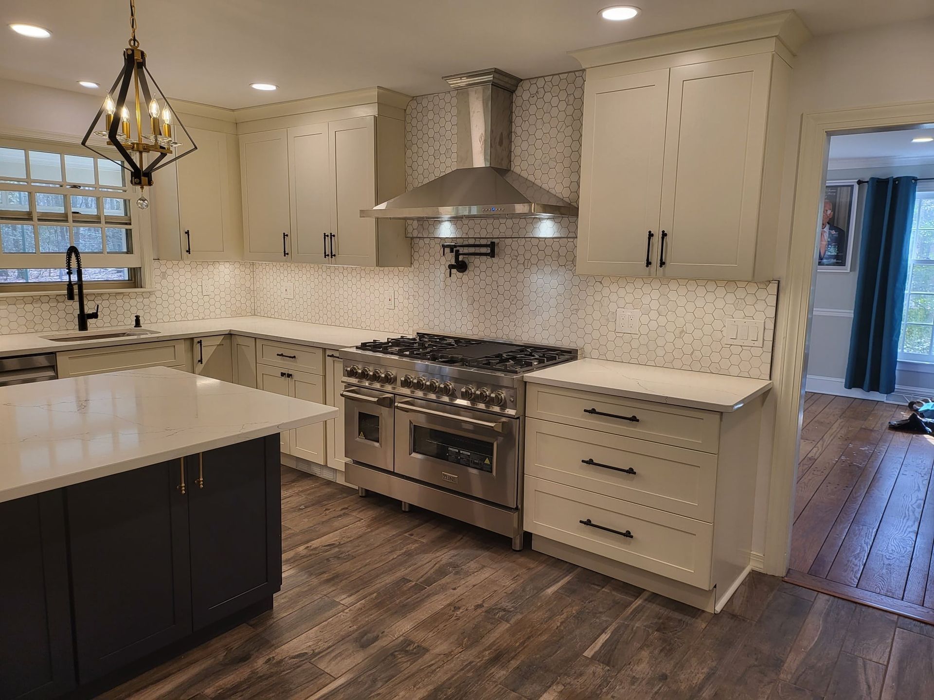Bright modern kitchen with white cabinets, marble backsplash, dark island, and stainless steel stove.