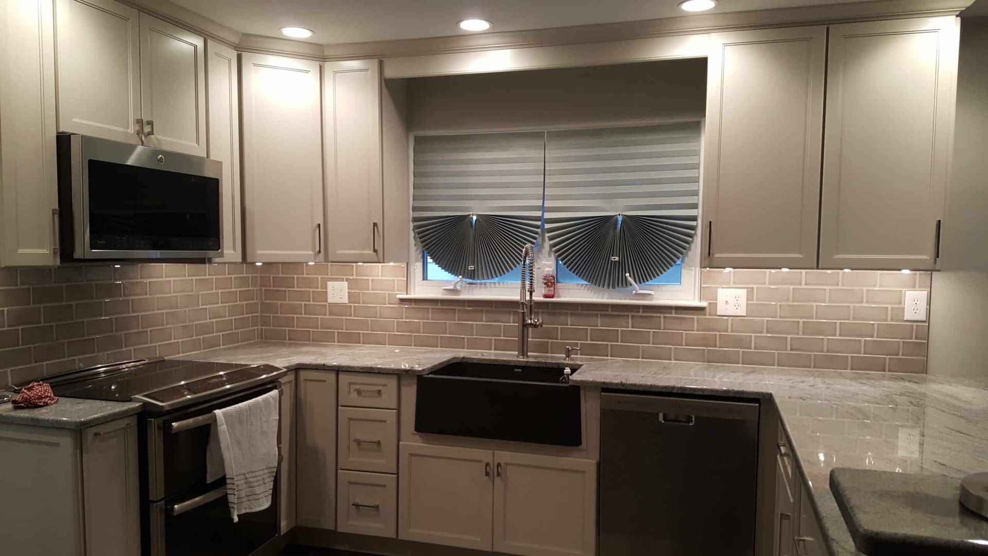 Modern kitchen with beige cabinets, tiled backsplash, sink under window, and stainless appliances