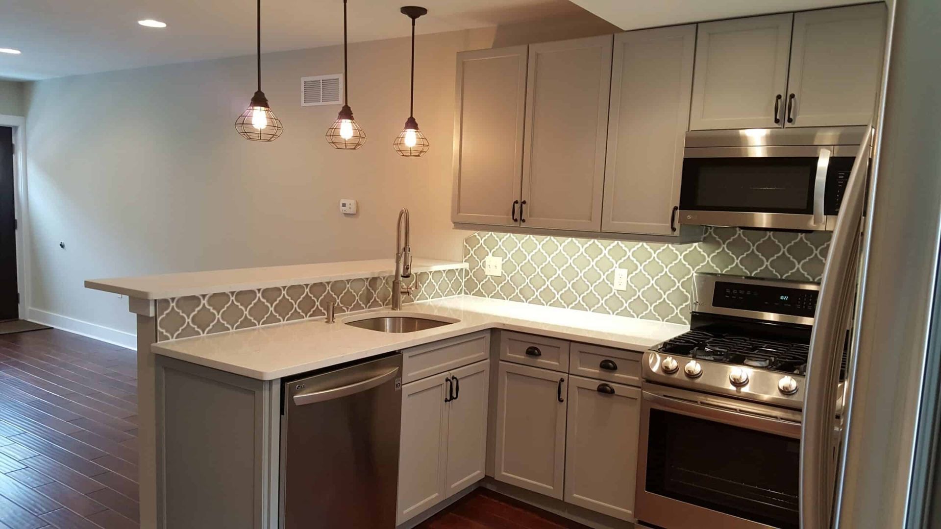 Modern kitchen with white cabinets, stainless steel appliances, pendant lights, and a tiled backsplash.