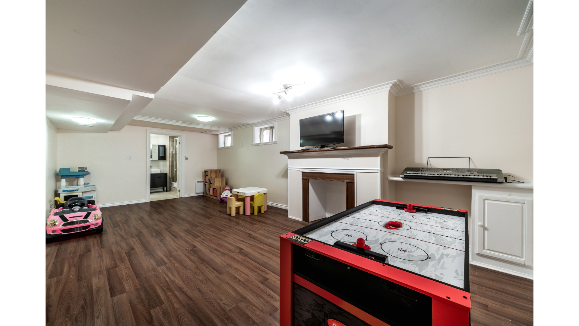 Basement rec room with dark wood floors, fireplace, TV, and toy play area.