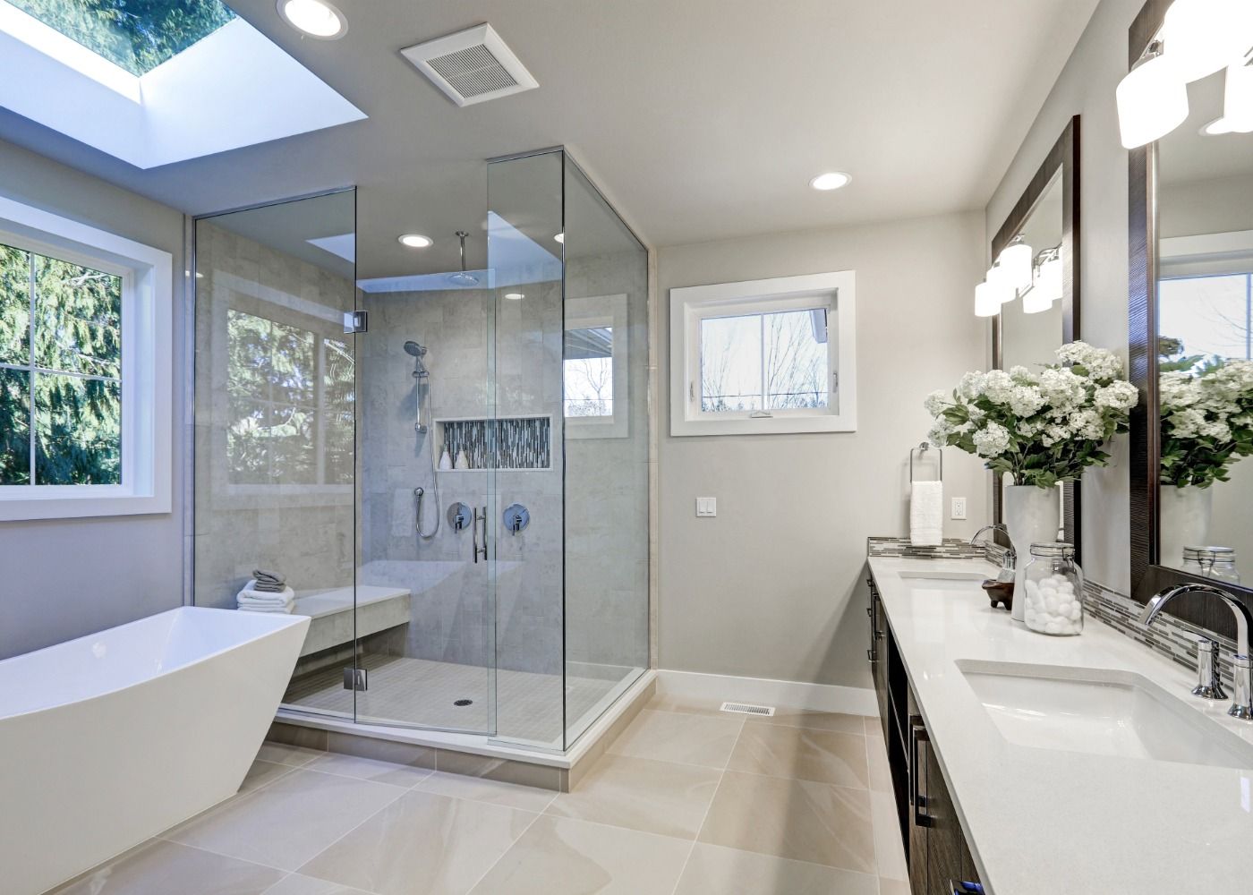 Modern bathroom with glass shower, freestanding tub, double vanity, and large windows