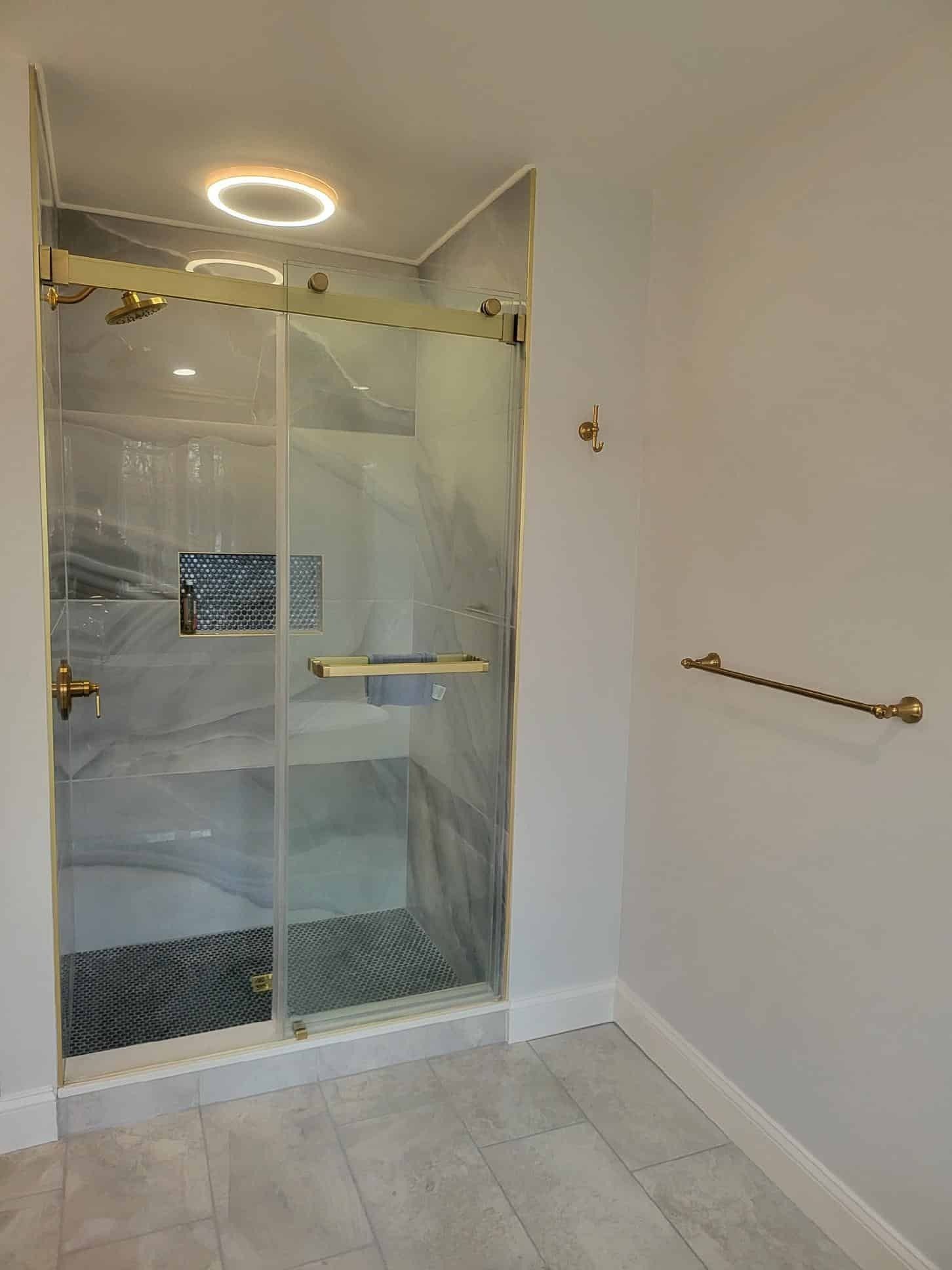 Accessible bathroom with glass shower enclosure, white tile floor, and grab bar on the right wall