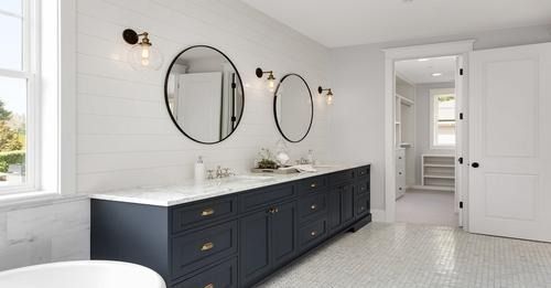 Modern bathroom with navy double vanity, round mirrors, wall sconces, and white tile floor