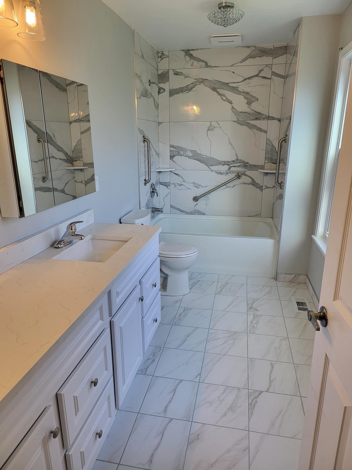 Modern bathroom with marble tile shower, double vanity, large mirror, and bright windows
