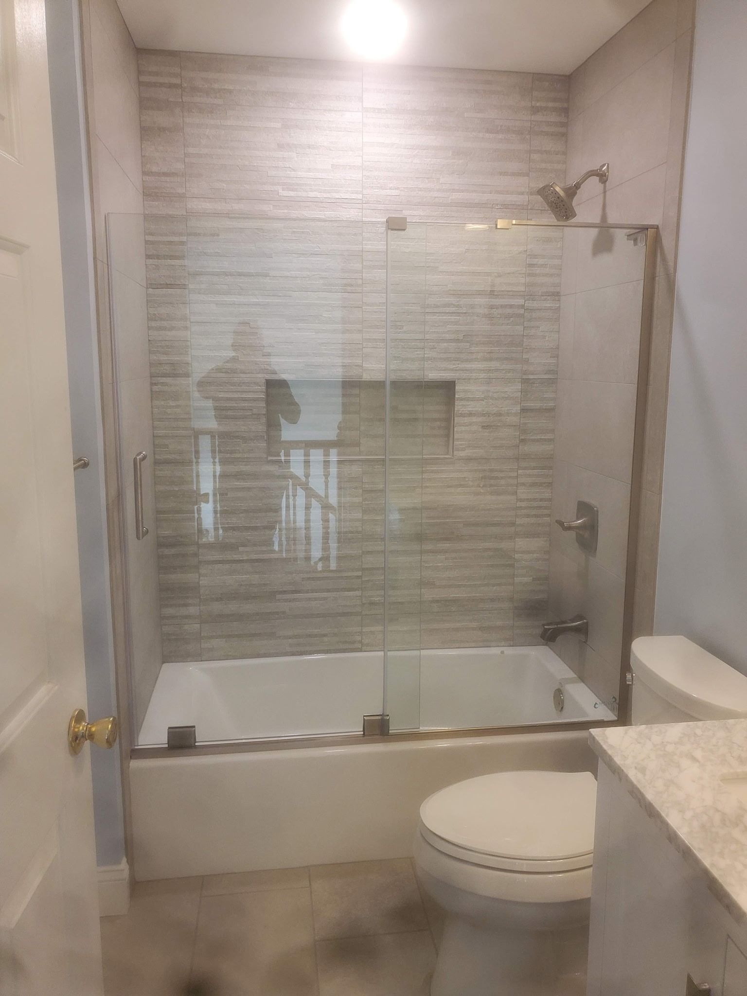 Bathroom with glass-enclosed shower over tub, white toilet, and light stone countertop.