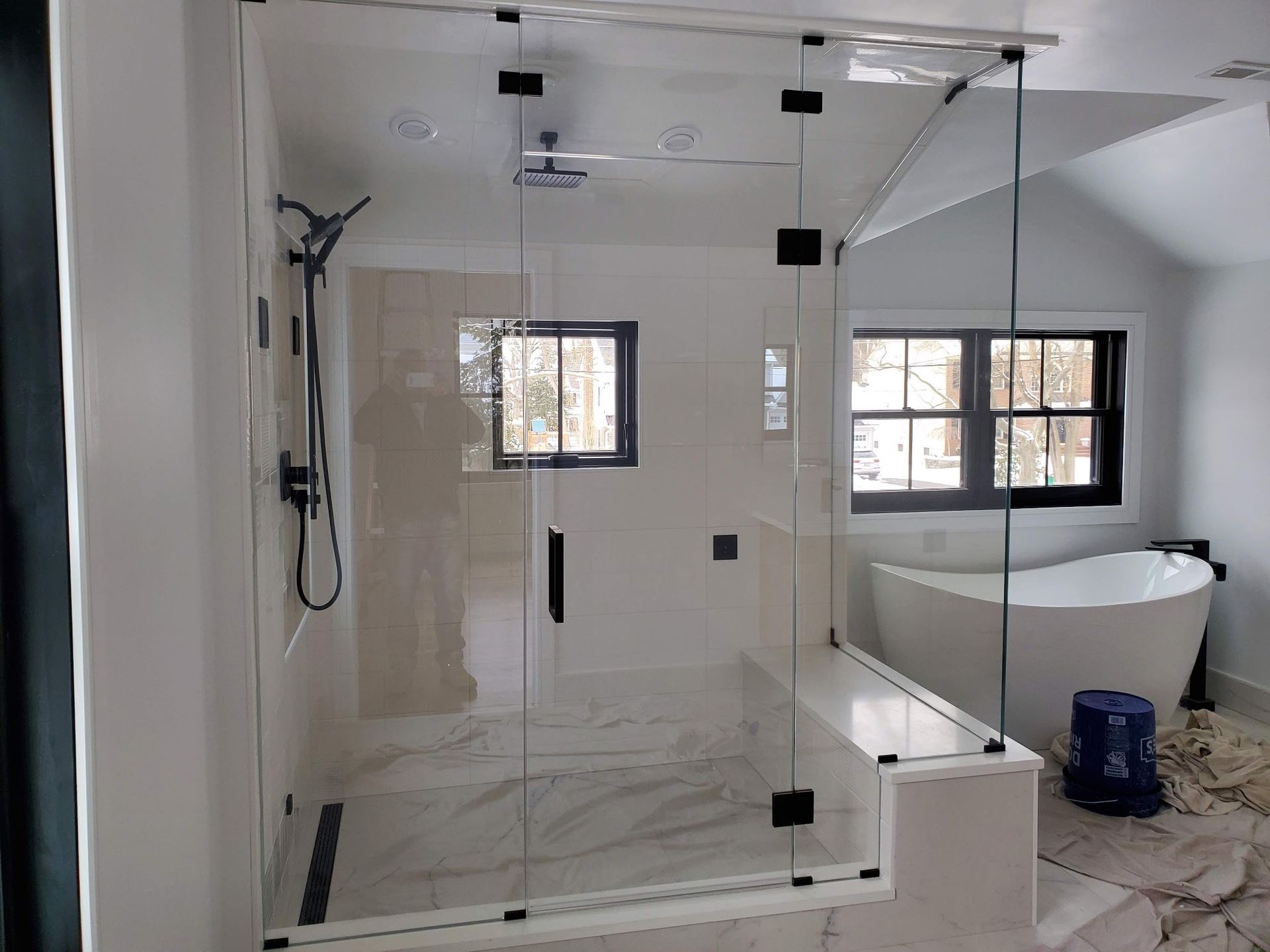 Modern bathroom with glass shower enclosure, white tile, and a freestanding tub by windows