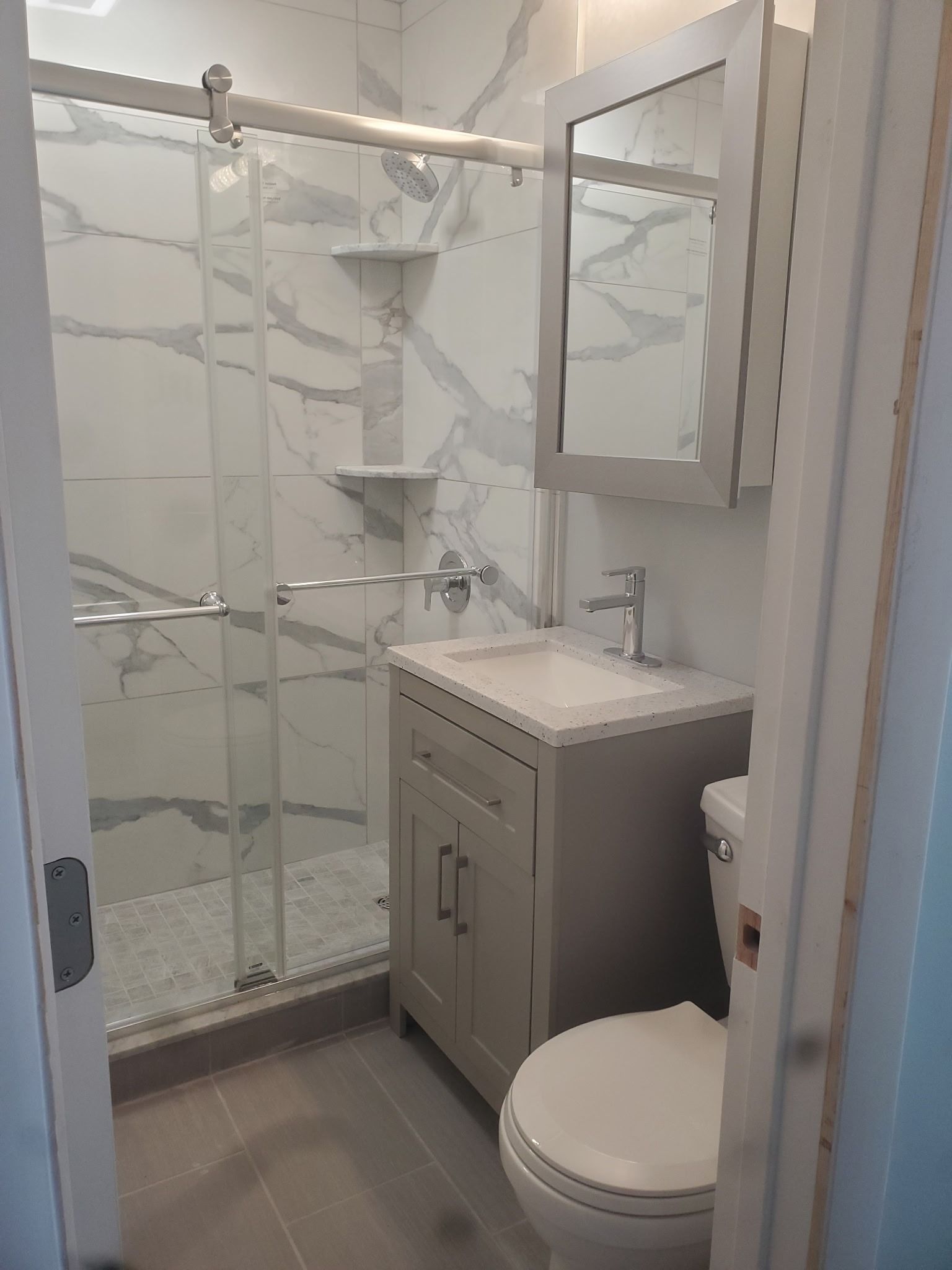 Small white bathroom with glass shower, gray vanity, and toilet.