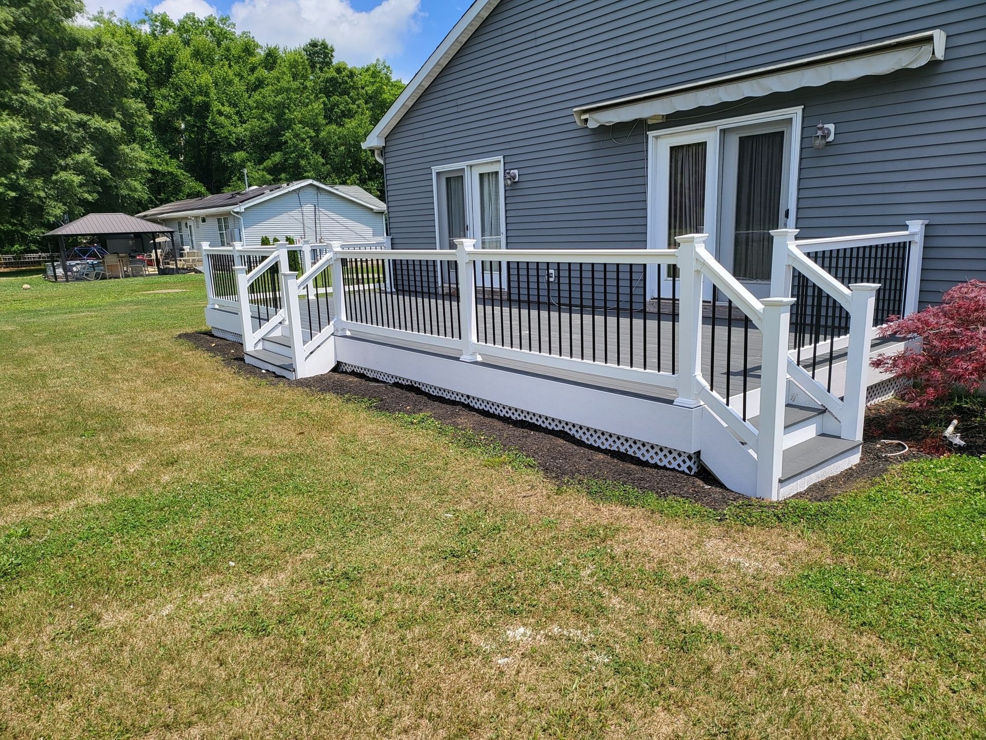 Gray house with white ramp and deck on a grassy yard under a blue sky