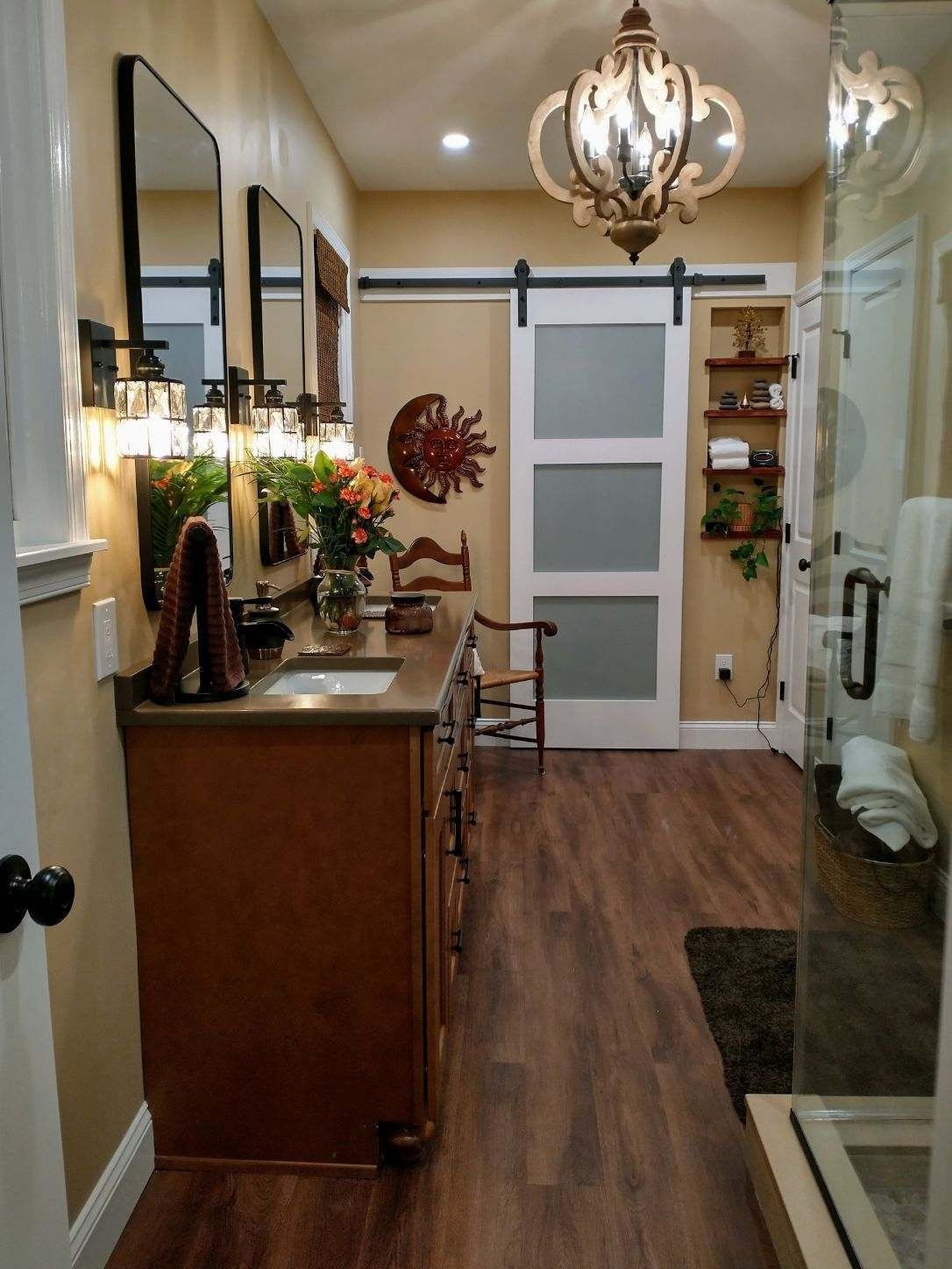 Narrow hallway with wood flooring, console table, chandelier, mirror, and white door at the end.