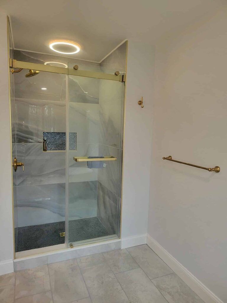 Glass shower enclosure with marble-look tile, light gray floor, and a wall towel bar