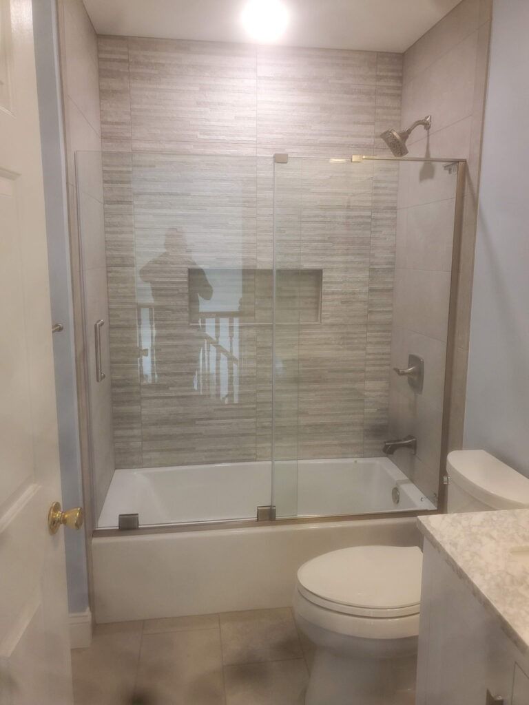 Modern bathroom with glass-enclosed shower over bathtub, toilet, and vanity counter