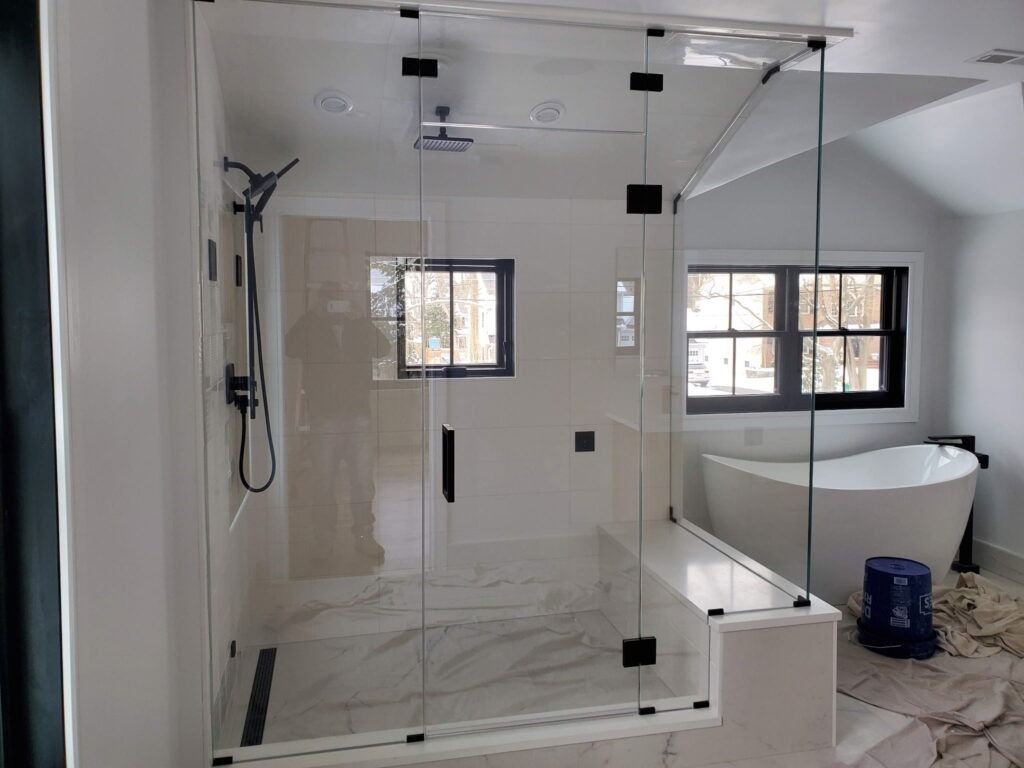Modern glass shower with white tile, marble floor, and freestanding tub in a bright bathroom