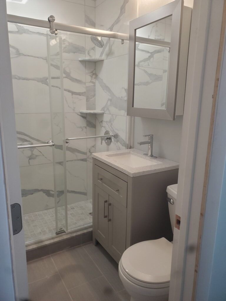 Small tiled bathroom with glass shower, vanity sink, mirror cabinet, and toilet.