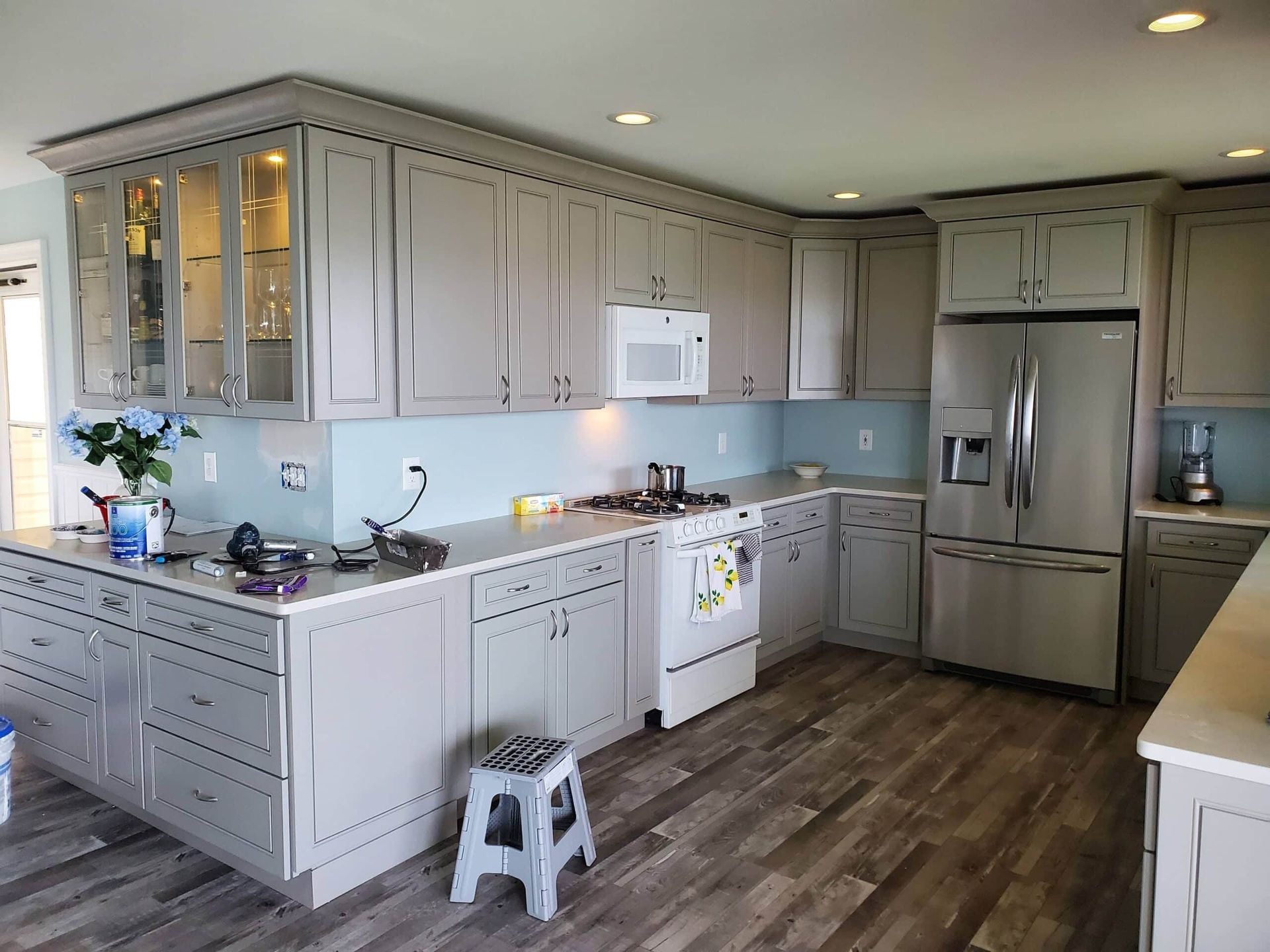 Bright kitchen with white cabinets, stainless fridge, light blue walls, and wood-look flooring