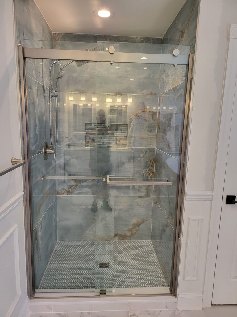 Glass shower enclosure with chrome fixtures and white tile in a bright bathroom
